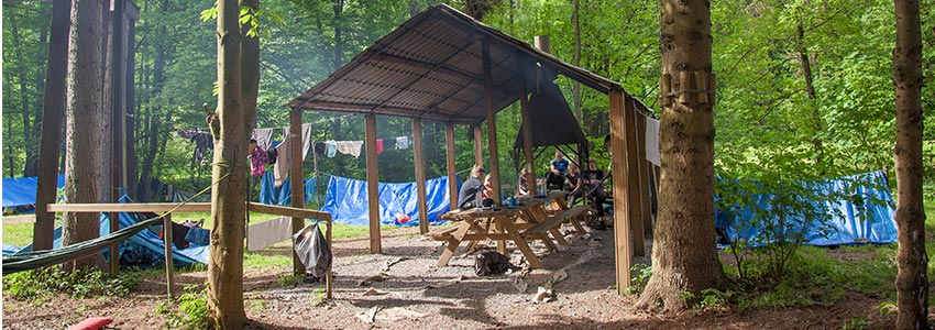 Bivakterrein met overkapping en overdekte kampvuurplek om te kamperen naast een beekje